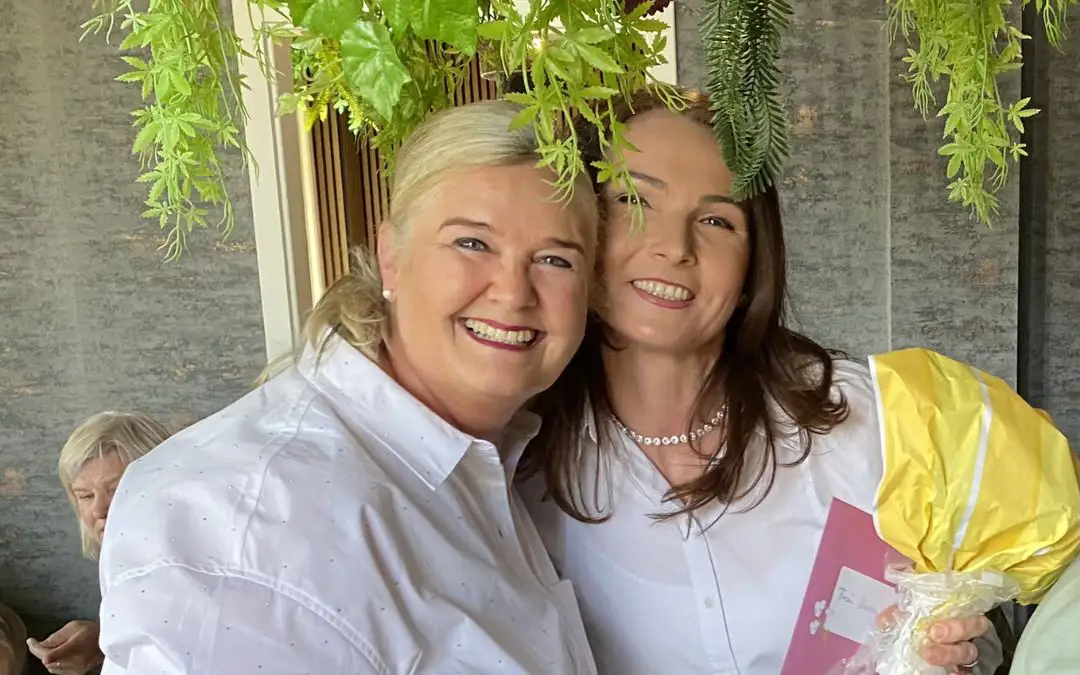Frau Kaufhold mit einer weiteren Kollegin unter grünen Pflanzen – beide strahlen mit Geschenk in der Hand.